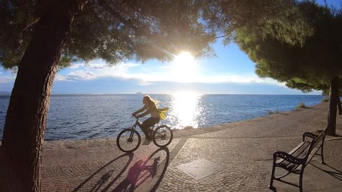 Young woman riding her bike on a walkway by the sea in sunshine 库存视频