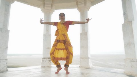 A wide shot of a Indian folk dancer dancing elegantly in a white marble temple located on a hilltop. A movement shot of a beautiful woman in traditional yellow sari performing classical dance form