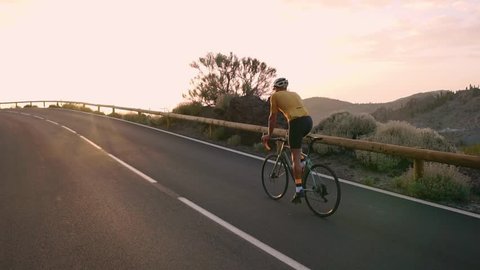 Man bicyclist in yellow t-shirt rides a mountain bike at sunset on the highway