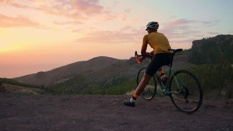 A tourist on a Bicycle admires the sunset from the top of the mountain