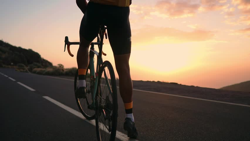 Man cyclist in a yellow t-shirt in the mountains watching the sunset. Resting after a workout, iron man. The view from the back