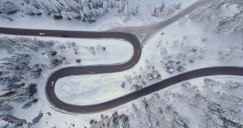 Overhead vertical aerial above hairpin turn road with cars,woods snowy forest.Sunset or sunrise.Winter Dolomites Italian Alps mountains outdoor nature establisher.4k drone flight establishing shot