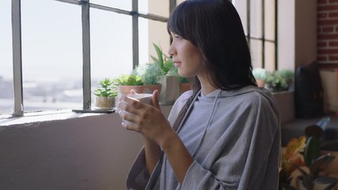 beautiful young asian woman drinking coffee at home enjoying relaxed morning looking out window planning ahead thinking contemplative female in trendy apartment