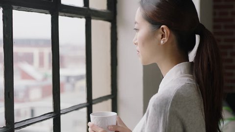 portrait beautiful asian woman drinking coffee at home smiling happy enjoying successful lifestyle looking out window planning ahead relaxing in cozy apartment loft