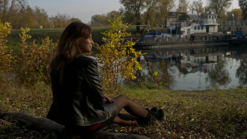 Young woman at fall outdoors, sitting at log, slow motion, shallow depth of field