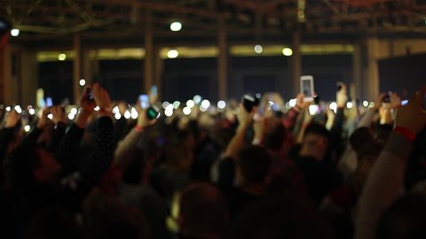 People waving hands with smartphones with flashlight. Live music concert. Slow motion, steadicam shot
