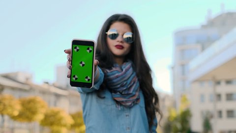 Young woman showing smartphone with green screen. Attractive young girl showing smart phone with chroma-key, green screen