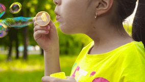 Little girl blowing soap bubbles in park. Closeup video