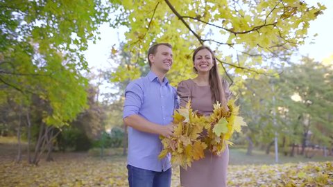 happy woman and man are throwing dry yellow foliage up and smiling in picturesque park in fall day