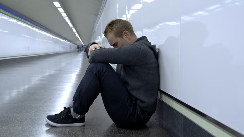 Miserable jobless young man crying Drug addict Homeless in depression stress sitting on ground street subway tunnel looking desperate leaning on wall alone in Mental disorder Emotional pain Sadness.