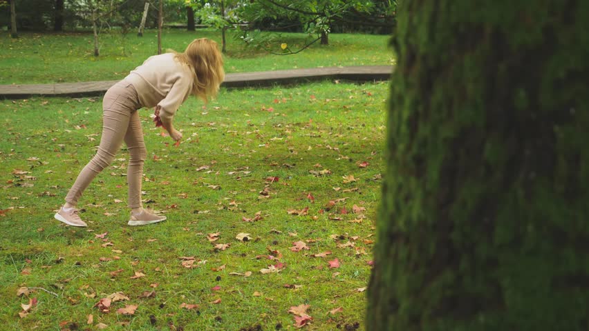 young blonde woman walks through the autumn park, she collects fallen maple colorful leaves