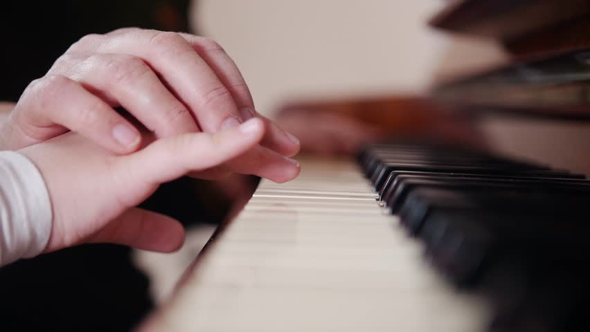 Music lesson. Child playing piano, elder teacher sits near and helps with playing. View from right side Royalty-Free Stock Footage #1018415827