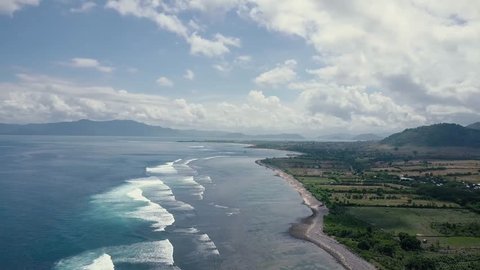 Aerial view: Waves and Panorama of  Indonesian Coastline, surf, bay, Tropical blue ocean, dry steep mountain cliffs, blue skies with clouds. Sea waves on reef to white sand beach. The mythical scenery
