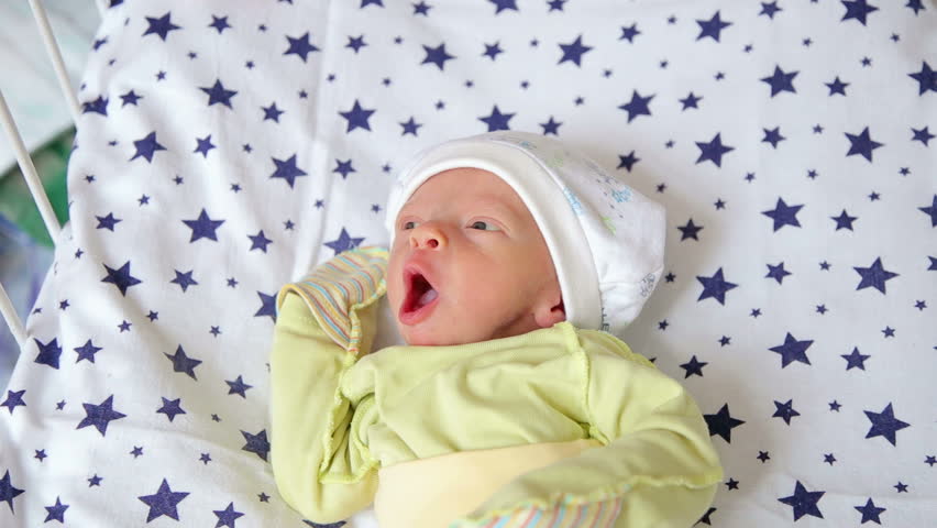 Portrait of a cute newborn baby in a hat in bed. Close-up. Newborn baby in the hospital lying in bed and looking at the new world.