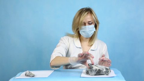 The girl laboratory technician examines samples of minerals.
A woman lab worker examines stones for analysis, the content of harmful asbestos.