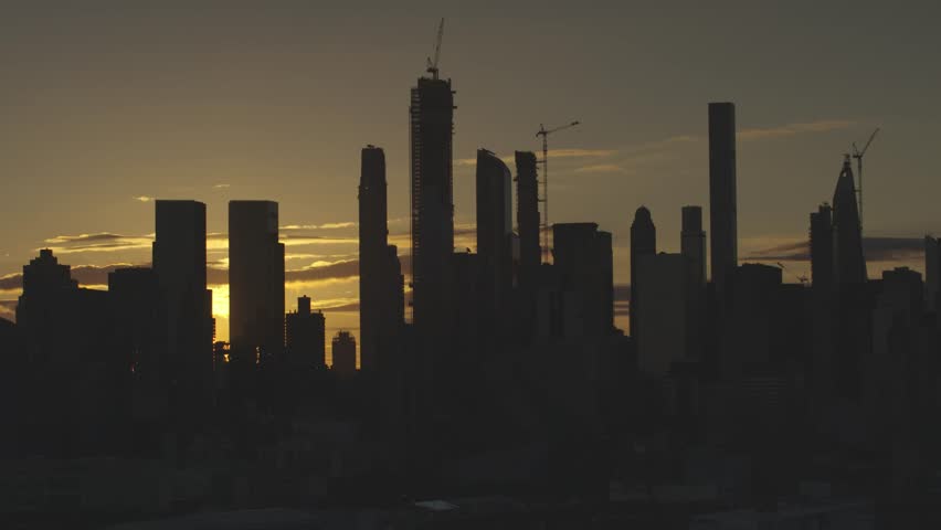 The Midtown Manhattan Skyline at Dawn.  Buildings are in silhouette the sun glows between the buildings.