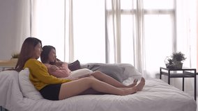 Slow motion - Happy Asian lesbian lgbt couple enjoy entertainment in living room. Beautiful women lying on a sofa with remote control and watching video and movie on television at home.
