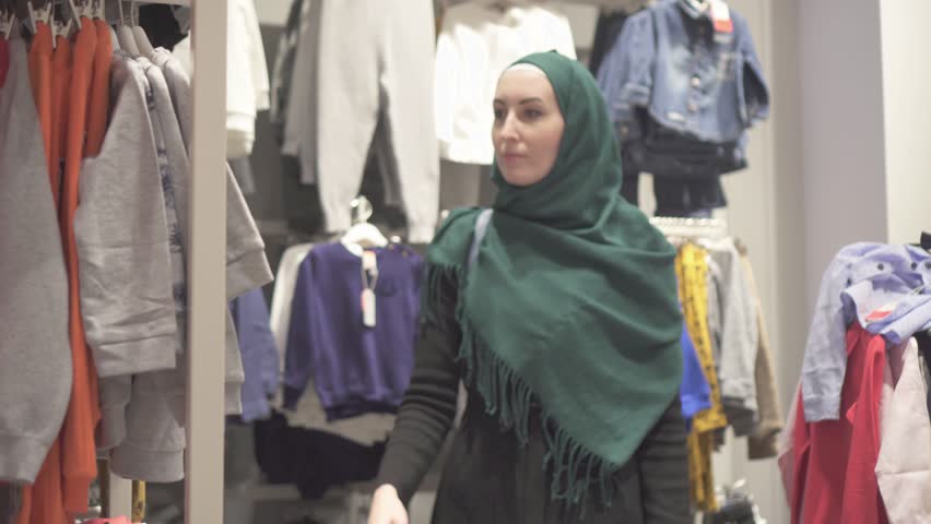 Muslim woman in a hijab and backpack chooses clothes in a children