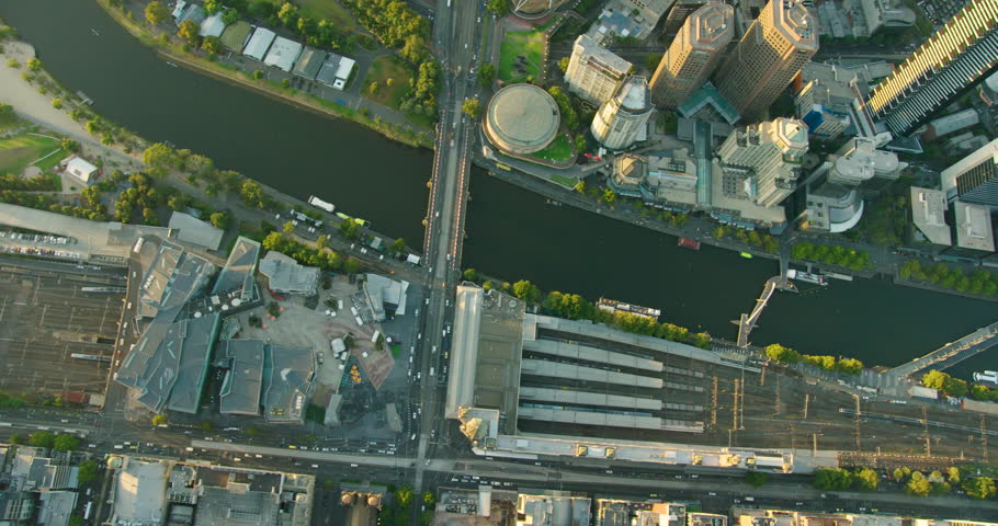 Aerial view Flinders Street Station and Federation Square at sunrise with passenger train travelling under bridge Melbourne Australia