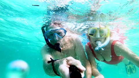Selfie portrait of retired Caucasian American couple having fun snorkeling waving to camera making video diary underwater Bahamas USA