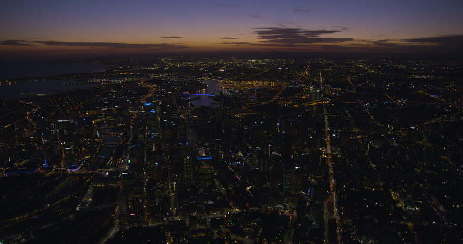 Aerial view at sunset across Melbourne CBD to Port Phillip Bay with illuminated streets and buildings Victoria Australia