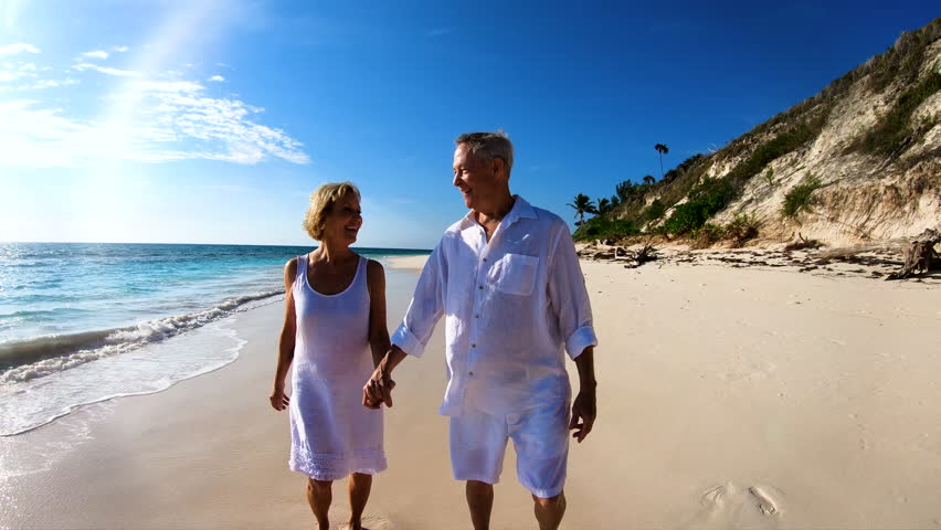 Healthy Caucasian American male and female seniors in white enjoying leisure dancing and walking in waves on beach outdoor Bahamas USA