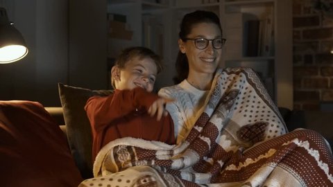 Happy mother and boy watching movies together on Christmas eve, they are sitting on the sofa and covering with a soft blanket
