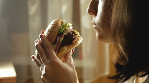 Young woman eating fast food, hamburger, close-up