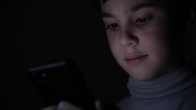 Happy Boy Enthusiastically Plays on a Smartphone in a Game in the Dark at Home. The face of the child is lit by a bright monitor