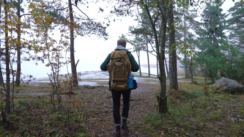 A middle-aged man walking on a rocky shore of the sea on a misty autumn morning and watching wildlife through binoculars. Slow motion