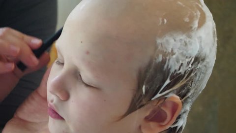 Young mother shaves head of blond boy with razor for preventing pediculosis. Good family tradition. Child is happy from hygiene procedures.