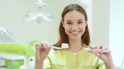 Woman doctor squeezing toothpaste on toothbrush. Stomatology assistant show cleaning teeth in dentist office. Close up female dentist squeezing toothpaste in dental clinic