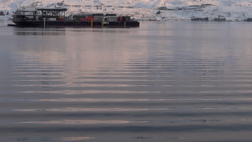 A barge travels through the water at the top of frame. (Alaska.)