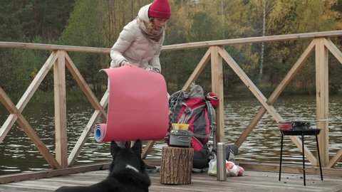 A woman tourist sits on the bridge near the river bank, near a dog, prepares food, gets things out of her backpack, picnic, outdoor activities and a healthy lifestyle, travel concept 4k