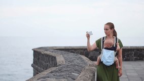 A young mother with a baby shoots on her hands looking at the ocean and shoots a stunning view of the waves on her smartphone