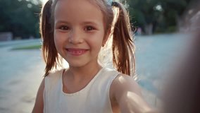 Face of pretty Caucasian little lady with wonderful smile. Beautiful Ukrainian child holding smartphone in hand, waving. Video chat. Outdoors. Park