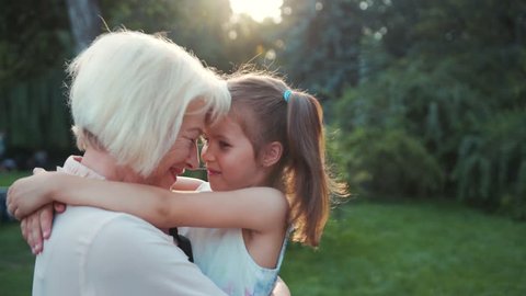 Happy good-looking Slavic grandma with blonde hair and cute preschooler hugging, looking at eyes of each others. Kind Ukrainian elderly and little girl smiling.