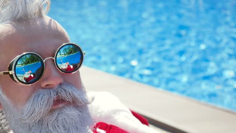Crazy person imitation Santa eat watermelon with passion and expression, have a cocktail lounging on sunbathing bad. Celebrate the life on the beach. Funny successful hipster at travel like a paradise