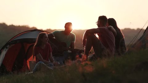 Silhouette of four friends on sunset light, actively communicating and laughing by their tourist tents. True friendship, adventure time, leisure. Camping, hiking, tourist concept