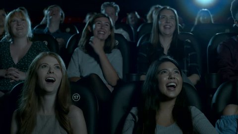 Movie theatre audience burst out laughing while watching a comedy film.