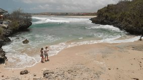 4K aerial flying drone video of young couple tourists on the wild rocky beach. Bali island.