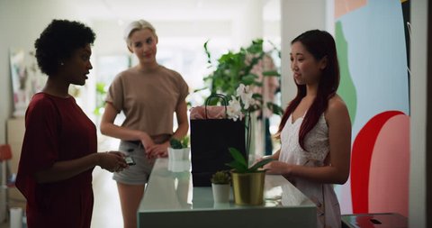 Two female friends purchasing item from store owner in interior boutique clothing store with soft day lighting. Medium shot on 4k RED camera.