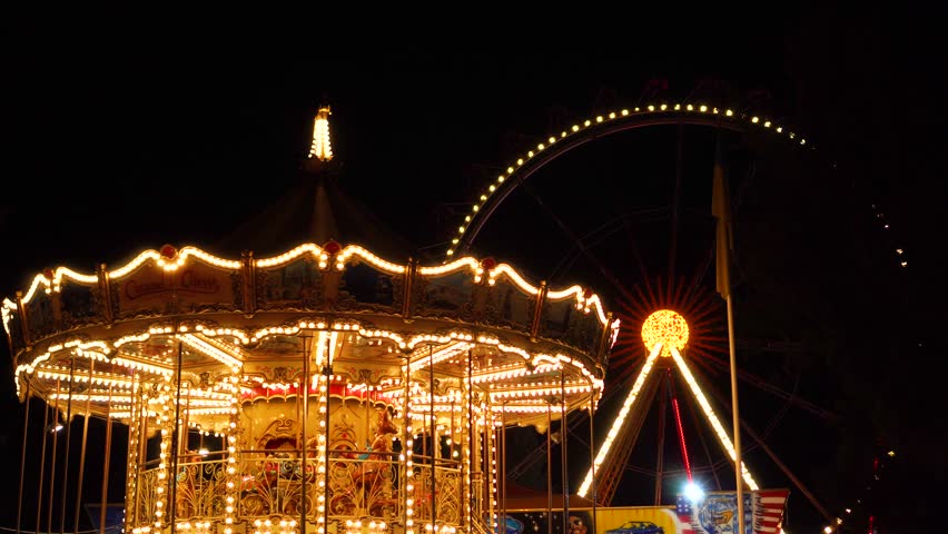 Flashing lights night illumination at amusement park carnival on vintage merry go round ferris wheel funfair attraction