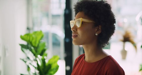 Stylish black woman taking pair of yellow sunglasses and trying them on in interior boutique clothing store with soft day lighting. Close up shot on 4k RED camera.