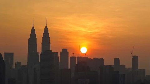 Silhouette of Kuala Lumpur city skyline with sun a giant orange ball rising amidst the skyscrapers.