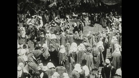 1930s: Men and women crowd and dance around statue of cow. Men and women frolic and dance.