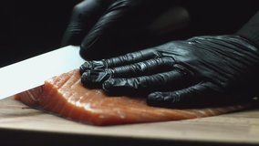 Close-up of sushi chef in gloves slices fresh salmon at sushi bar. Slicing salmon fillets