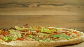 putting parmesan cheese on pizza with bacon and vegetables rotate on wooden table.