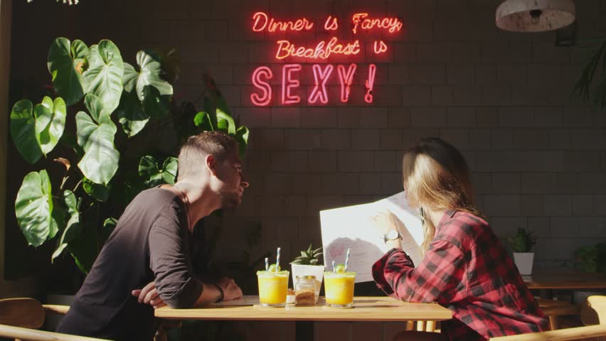 Young woman asking her boyfriend for advice what to order for lunch sitting in cafe