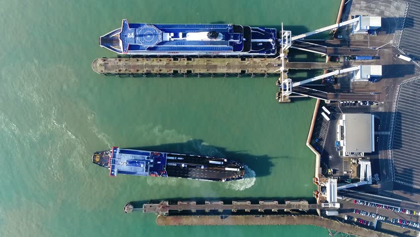 Aerial top down view of ferry moving backwards to dock and embark this vessel carries lorries cars and passengers across body of water ferries form part of the public transport systems 4k resolution